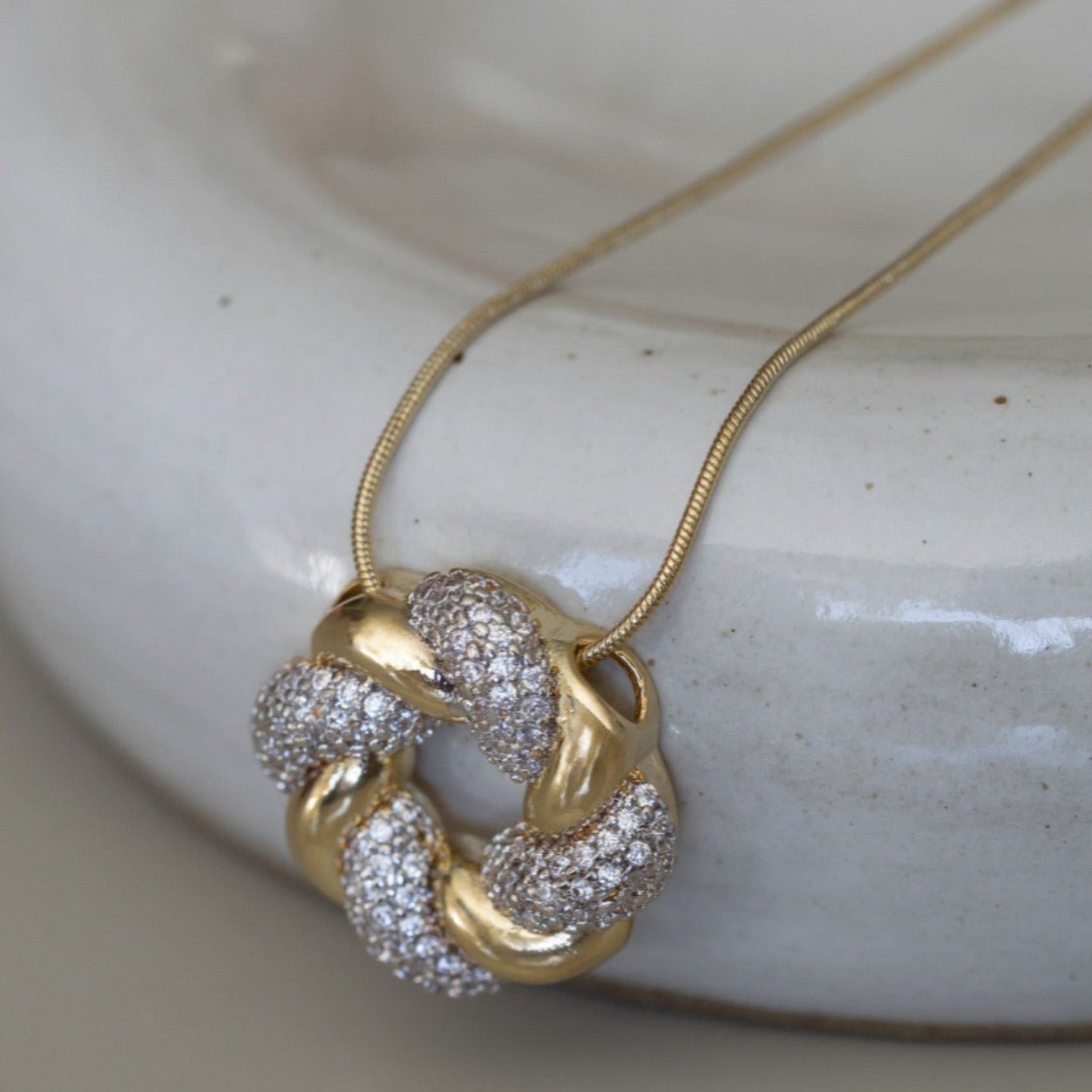 Close-up of gold twist pendant necklace with pavé detail on ceramic surface – Tara - Luiza Jewelry