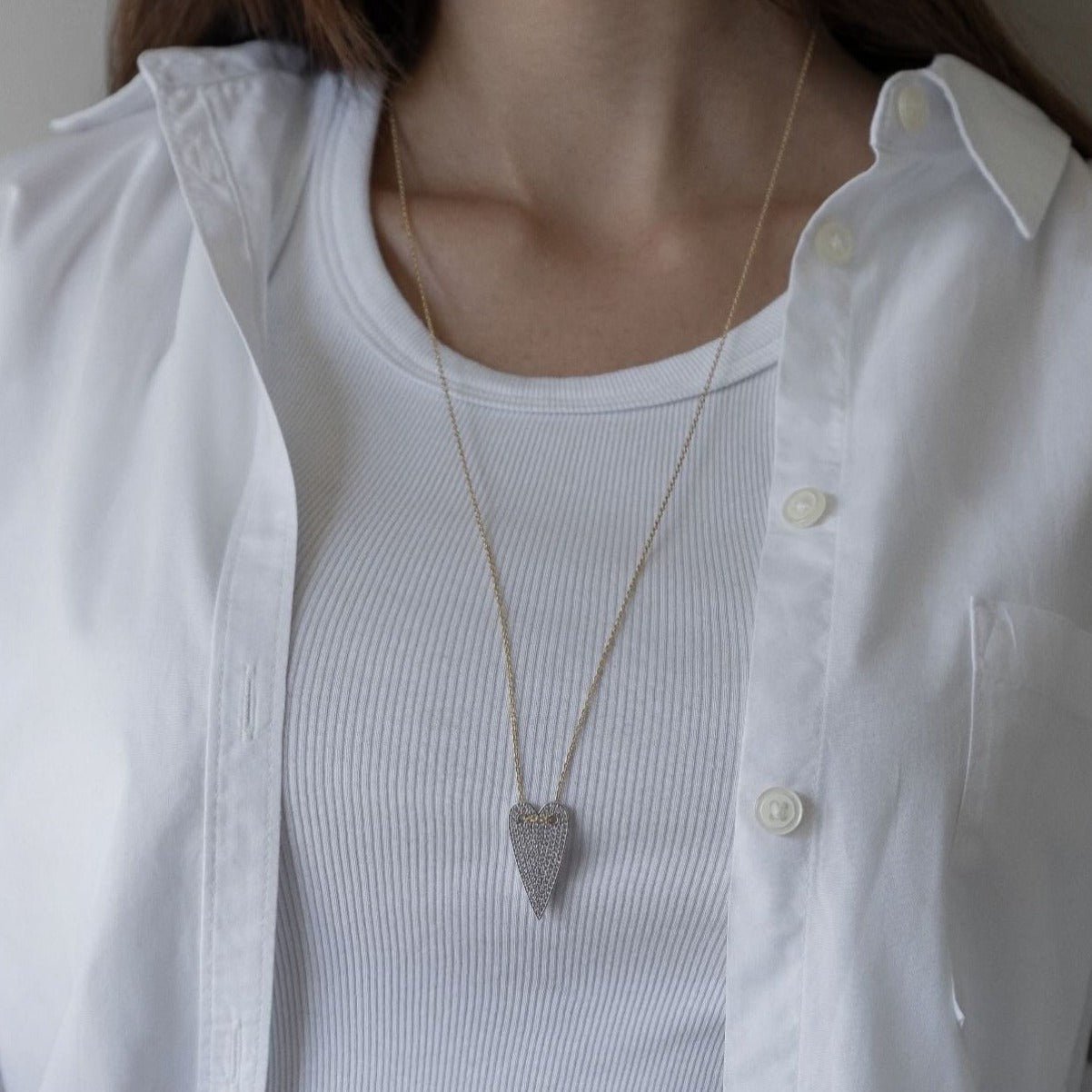 Celina necklace with long gold chain and smooth heart-shaped pendant, worn over beige fabric - Luiza Jewelry