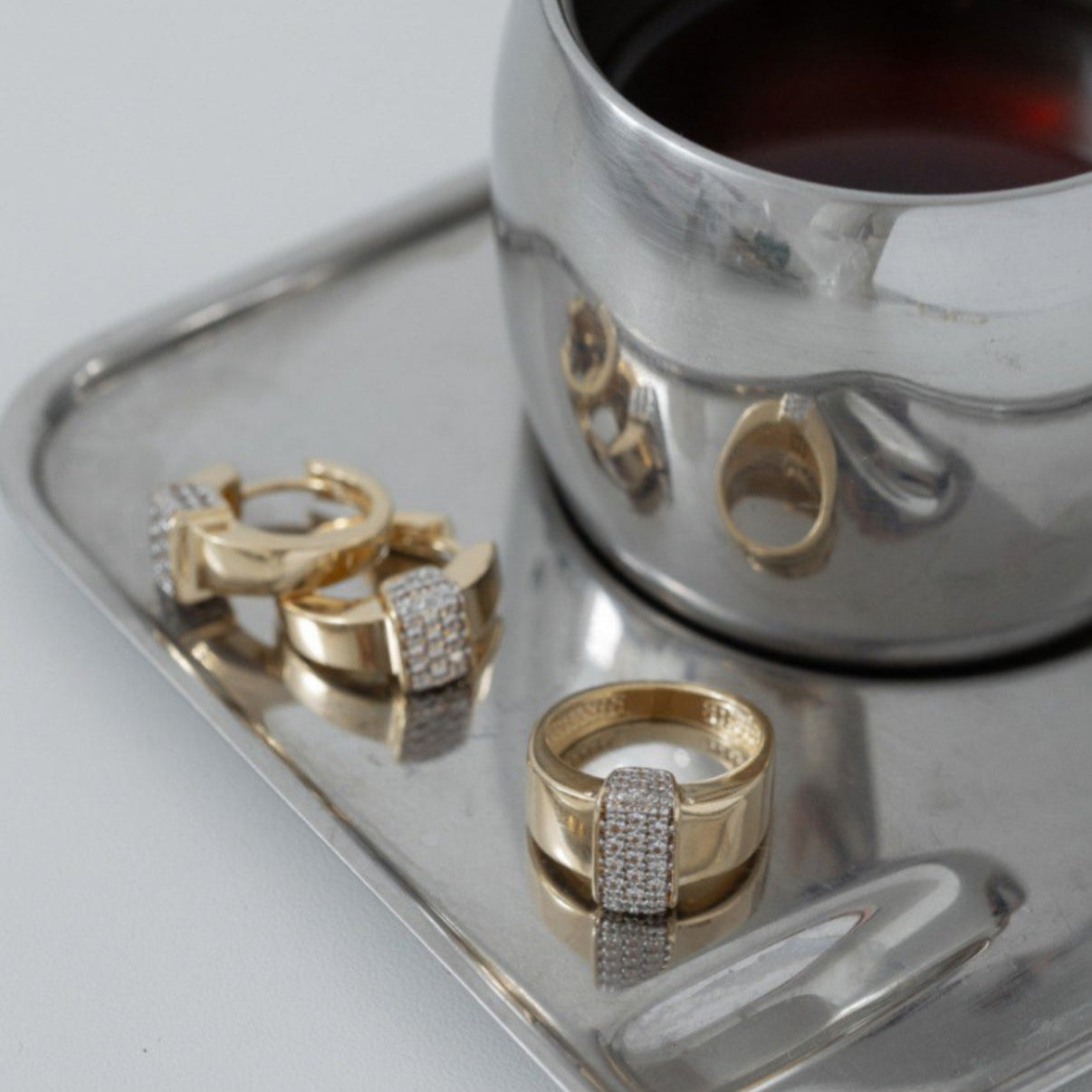 Gold rings with diamonds on a silver tray next to a silver cup.
